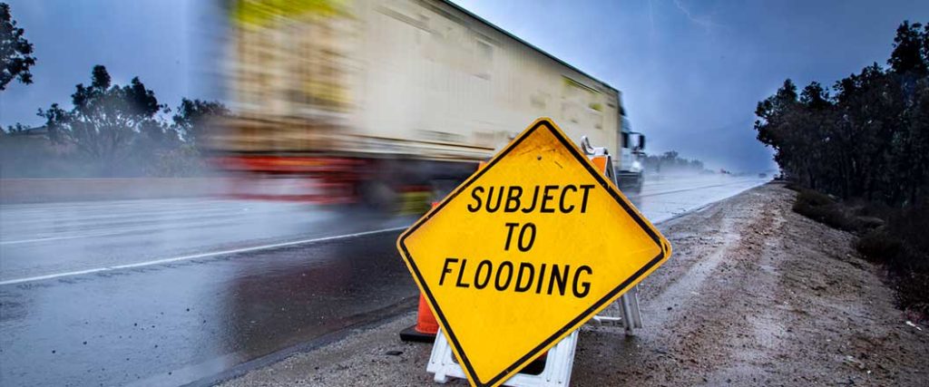 A semi truck passing by a sign that says subject to flooding
