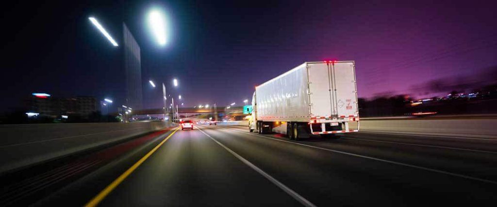 A rear-facing image of a semi truck driving at night.