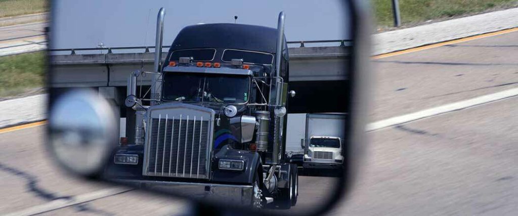 A semi truck's reflection in a rearview mirror.